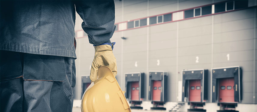 Worker holding a hard hat in front of a row of loading dock doors