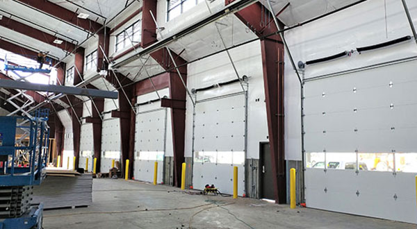 Warehouse interior with a row of white sectional doors and a scissor lift
